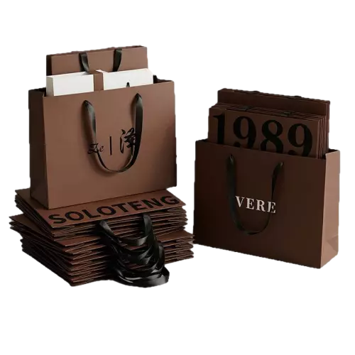 These premium special craft paper bags come with elegant matte coffee brown surface for a high end minimalist look. Durable smooth black ribbon handles offer comfortable grip and excellent weight bearing performance. Thick sturdy craft paper keeps the bag upright and resistant to deformation. You are free to customize logo brand name slogan and special characters on the surface. Multiple size selections can meet different packing needs for clothing jewelry cosmetics and boutique retail goods. These timeless shopping bags are perfect for brand store packaging and business gift use. Wholesale bulk orders are welcomed.