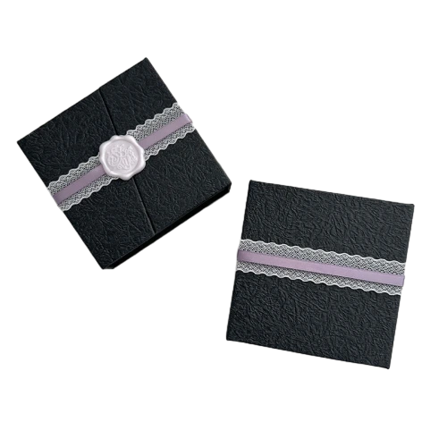 This vintagestyle square custom rigid box is constructed from thick hardboard and wrapped in distinctive crinkled textured black paper. It adopts elegant double door opening design with hidden magnetic closure for smooth opening. Decorative lavender satin ribbon matched with white lace band and custom wax seal ornament adds delicate romantic appeal. Inner foam or velvet inserts can be customized to hold jewelry trinkets and small luxury gifts. Its solid hard shell provides excellent protection during transit and retail display. It is an ideal premium packaging option for boutique brands and large volume wholesale orders.
