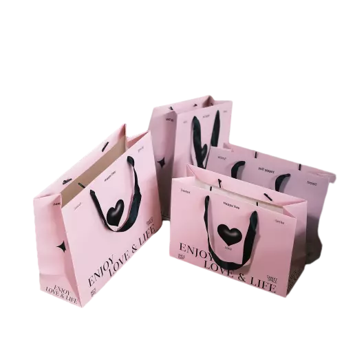These romantic themed paper gift bags are made of high quality matte pink paper printed with stylish heart graphic and warm life slogan. Soft durable black fabric ribbon handles bring comfortable touch and reliable load bearing performance. Multiple sizes are available for different packing requirements of cosmetics accessories and surprise gifts. Thick paper material helps the bag keep firm upright shape and avoid collapse. You can replace the original pattern and words with your own custom logo brand slogan and artwork. These lovely pink gift bags fit perfectly for Valentine gifts birthday favors boutique retail and daily gift giving. Wholesale bulk orders are welcomed.