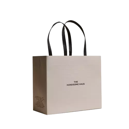 These minimalist brand paper shopping bags are made of high quality thick beige paper with soft matte finish. Durable wide black fabric ribbon handles provide comfortable grip and strong load bearing capacity. Simple centered brand text printing creates a clean modern look suitable for fashion retail stores. The wide horizontal base keeps the bag standing firmly on flat surfaces. Full custom printing service is available for your unique logo brand slogan and surface artwork. These neutral tone tote bags work perfectly for clothing shops cosmetic boutiques and brand gift packaging. Wholesale bulk orders are welcomed.