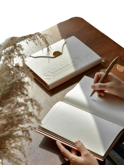 These elegant hardcover notebooks adopt premium textured PU leather covers with delicate embossed letter details and a unique envelope style flap fitted with gold magnetic buckle, presenting a minimalist luxury aesthetic suitable for both business and personal scenarios. Built with a practical ribbon bookmark for quick page locating and thick premium lined inner pages that ensure smooth writing performance and effectively prevent ink bleedthrough, they are perfect for work planning, meeting minutes and daily journaling. The slim portable design fits easily into handbags for on the go use, and the cover supports custom logo printing to satisfy brand personalization demands. They serve as high-end stationery gifts for corporate clients and employees, ideal for boutique retail and bulk wholesale procurement.