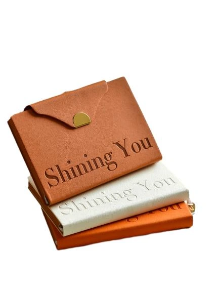These elegant hardcover notebooks adopt premium textured PU leather covers with delicate embossed letter details and a unique envelope style flap fitted with gold magnetic buckle, presenting a minimalist luxury aesthetic suitable for both business and personal scenarios. Built with a practical ribbon bookmark for quick page locating and thick premium lined inner pages that ensure smooth writing performance and effectively prevent ink bleedthrough, they are perfect for work planning, meeting minutes and daily journaling. The slim portable design fits easily into handbags for on the go use, and the cover supports custom logo printing to satisfy brand personalization demands. They serve as high-end stationery gifts for corporate clients and employees, ideal for boutique retail and bulk wholesale procurement.