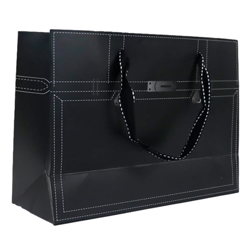 This rectangular special craft paper bag adopts elegant matte black surface with creative suitcase inspired design. White simulated stitch line patterns are printed on front and sides to mimic classic leather trunk texture. A decorative metal nameplate is fitted at center front for premium visual feel. Black woven ribbon handles with white edge stitching connect securely to bag body. Sturdy thick craft paper keeps the bag rigid and well shaped for heavy gifts. You can customize bag dimensions handle style printed stitch color metal tag design and brand logo. It fits well for luxury clothing footwear cosmetics perfume bottles and high end festival gift packaging.