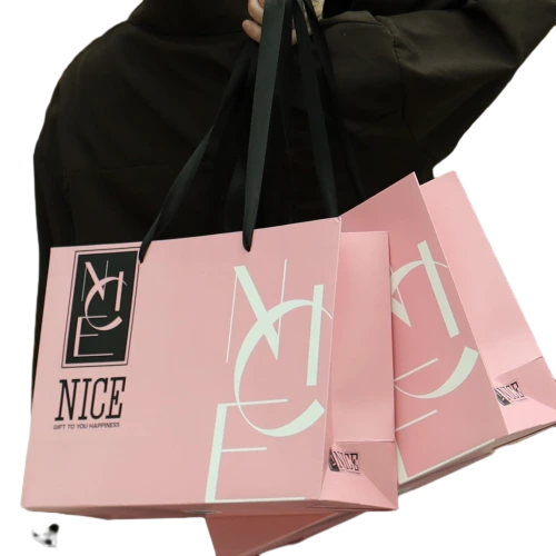 Special Craft Paper Bags feature trendy light pink surface decorated with modern abstract letter graphics and slogan NICE GIFT TO YOU HAPPINESS. Matching wide black ribbon handles are soft and sturdy for comfortable carrying. Thick premium craft paper keeps the bag rigid and holds shape well. The fresh stylish design fits fashion store cosmetic shop and clothing brand packaging. We support custom bag size base color printed text and brand logo. These paper bags are perfect for retail shopping birthday gifts and brand gift giving.