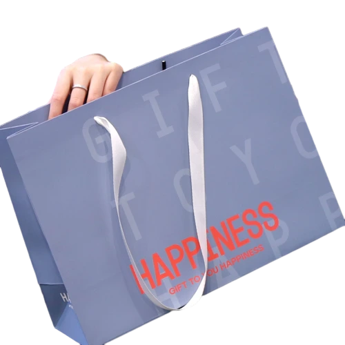 Special Craft Paper Bags adopt soft light blue base decorated with subtle faint background letters and striking red HAPPINESS slogan. White wide ribbon handles are smooth and durable for comfortable hand holding. Thick premium craft paper keeps the bag rigid and maintains neat shape. The gentle tone with eye catching text creates warm vibe for gift delivery. We support custom bag size base color printed text and brand logo. These paper bags fit birthday gifts cosmetic shop packing clothing boutique shopping and holiday gift sets.