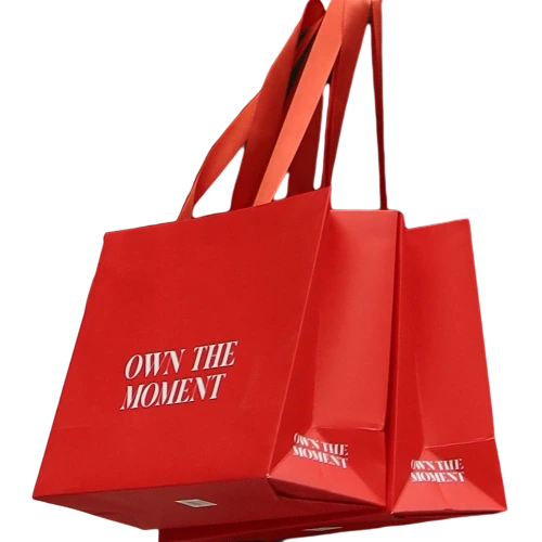 Special Craft Paper Bags feature striking solid bright red surface printed with elegant white slogan OWN THE MOMENT. Matching wide red ribbon handles are smooth and tough for comfortable carrying. Thick premium craft paper keeps the bag rigid and maintains tidy shape. The vibrant red tone delivers festive and stylish look for retail and gift giving scenarios. We support custom bag size base color printed text and brand logo. These paper bags are suitable for fashion stores cosmetic shops birthday gifts and holiday gift sets.