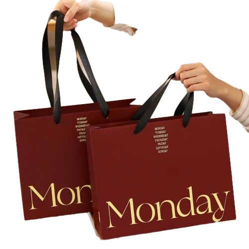 Special Craft Paper Bags feature elegant burgundy surface decorated with delicate gold week letter print including large Monday font. Smooth black wide ribbon handles bring comfortable hand touch and strong load bearing capacity. Thick premium craft paper keeps the bag rigid and holds shape nicely. Retro warm red tone combined with gold printing creates refined fashion texture for brand retail and gift giving. We support custom bag size base color printed text and brand logo. These paper bags work perfectly for fashion boutique shopping cosmetic packaging birthday gifts and holiday gift sets.