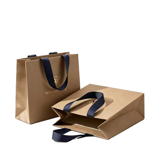 Special Craft Paper Bags adopt premium matte khaki paper with subtle fine texture surface. Matching navy blue wide satin ribbon handles are soft sturdy and comfortable to hold. Custom gold foil hot stamping logo and brand name are printed on front for luxury understated branding. Thick rigid craft paper keeps the bag upright and holds shape well during shipping. The flat foldable design saves storage space and logistics cost. We support custom bag size handle color foil logo and surface finish. These paper bags are ideal for clothing stores jewelry packaging boutique shopping birthday gifts and holiday gift sets.