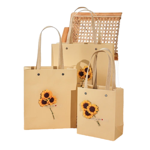This set of coated art paper tote bags comes in three practical sizes with soft beige outer surface. Woven ribbon handles are reinforced with metal rivets at both sides for comfortable hand carrying and strong load bearing. Artificial sunflower ornaments with small printed label tags are attached on the front to deliver warm and healing atmosphere. Thick rigid paper body keeps the bag shape well during transport. You can customize bag size handle color flower decoration style label text and brand logo. It fits well for birthday gifts wedding favors holiday presents snack sets dried flower souvenirs and boutique retail packaging.