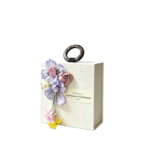 This delicate custom rigid magnetic gift box features elegant cream speckled paper surface. It is fitted with a natural wooden ring handle on the top for convenient carrying. Beautiful handmade fabric flower decorations are attached on the front side together with a printed paper waist band with warm greeting words. Hidden magnet ensures secure lid closure. Thick high quality rigid cardboard keeps the box shape stable. You can customize box texture artificial flower style handle design slogan content and brand logo. It fits well for wedding favors bridal shower gifts birthday presents guest souvenirs and high end celebration gift packaging.